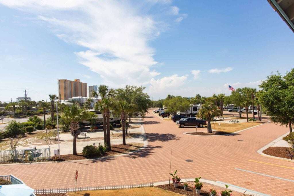 A parking lot with several cars and palm trees under a blue sky, with a tall building and an American flag visible in the background.